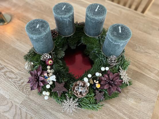 Adventskranz aus dunkelgrünen Tannzweigen, grünen Kerzen und verschiedener Deko: Sterne, Tannenzapfen, goldene Kugeln