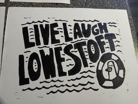Black-and-white lino print with the phrase “LIVE LAUGH LOWESTOFT” in big bold letters surrounded by wavy lines. On the right, a cartoon seagull sits inside a rubber ring.