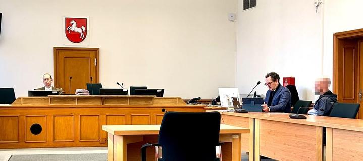 Konferenzraum mit Tischen und Stühlen, mehrere Personen sitzen an den Tischen. Im Hintergrund ein Wappen an der Wand.