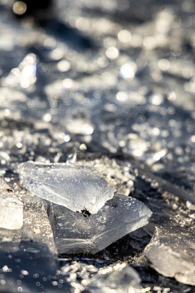 Zerbrochenes Eis auf einer gefrorenen Pfütze 
Der Hintergrund verschwimmt 
Lichtkreise funkeln