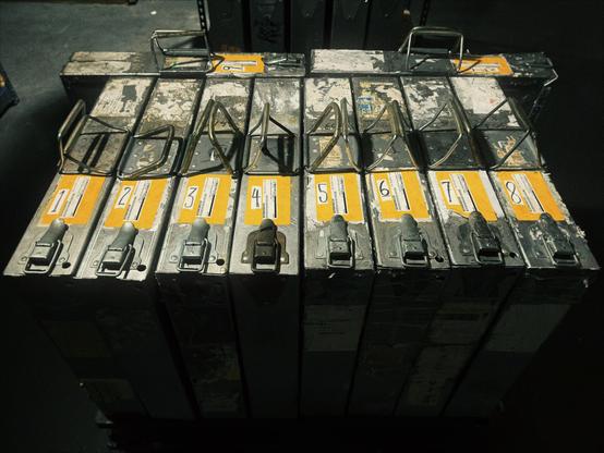 Large film canisters, each labeled a number from "1" to "10," sit on a small cart in a film storage room of the Hollywood Theatre, with one of the reels being held for the camera.