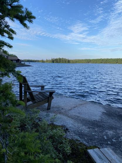 A bear chair sits on a slab of flat rock overlooking a lake