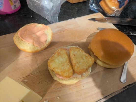 a photo of a burger bun with 2 hash browns on its bottom half, alongside its top half smothered in pink sauce.