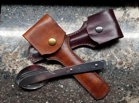 Tan and mahogany leather cases for travel flatware sets. One of the flatware sets is removed from its case and is lying on top of it. They are placed on a piece of grey marble.