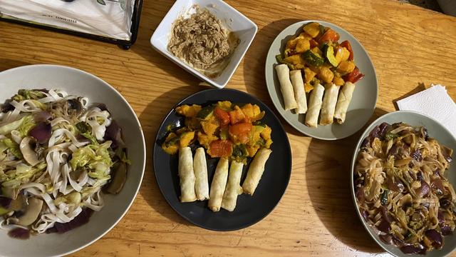 Two plates of rice noodles, mushrooms, red onion, cabbage and leek. One of the plates have gochujang sauce. two more plates with five spring rolls each and a mix of roasted veggies, such as courgette, Hokkaido pumpkin and bell peppers. A little bowl with natto.