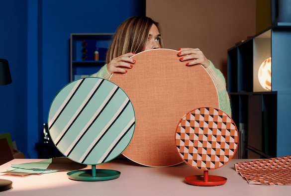 Une femme tenant des objets décoratifs de couleurs vives, avec des motifs géométriques, devant un fond coloré, évoquant un esprit créatif et moderne.