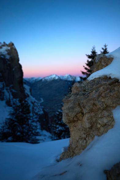 A small rock with snow ontop and a beautiful dawn blurred in the background.