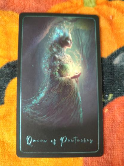 Card from the Tarot of the Sacred Kingdoms deck.
Queen of Pentacles.
A woman in the woods dressed in green. It is dark outdoors but she has a shining plant on her hands that lends her some radiance.