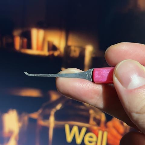 Photo of a hand holding a lockpick, with the thumb and the index finger on the handle of the pick, and the middle finger on the shaft of the pick to stabilise it