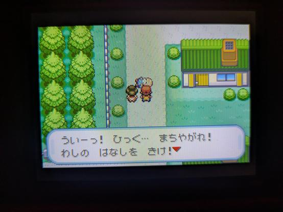 A screenshot from the Japanese-language Pokémon video game LeafGreen for GBA. The player character is standing next to an older male NPC on a path between a forest and a green-roofed building. A dialogue box at the bottom contains the Japanese text: "ういーっ! ひっく... まちゃがれ! わしの はなしを きけ!" which roughly translates to "Whee! Hic... Wait up! Listen!"