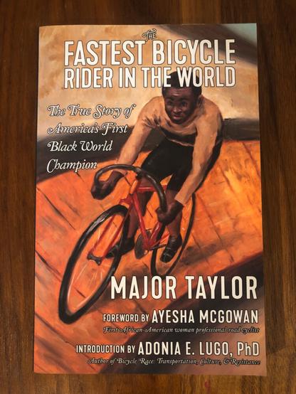 Book cover with a painting of a Black man on a track bicycle. The Fastest Bicycle Rider in the World. The True Story of America's First Black World Champion. Major Taylor. Foreward by Ayesha McGowan. Introduction by Adonia E. Lugo, PhD.