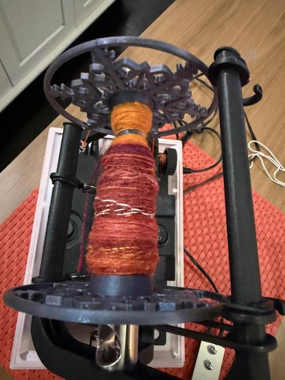 Bobbin with the singles from the first of 3 spindles chain plied orange at top, red at bottom. On an EEW 6.1 e spinner.