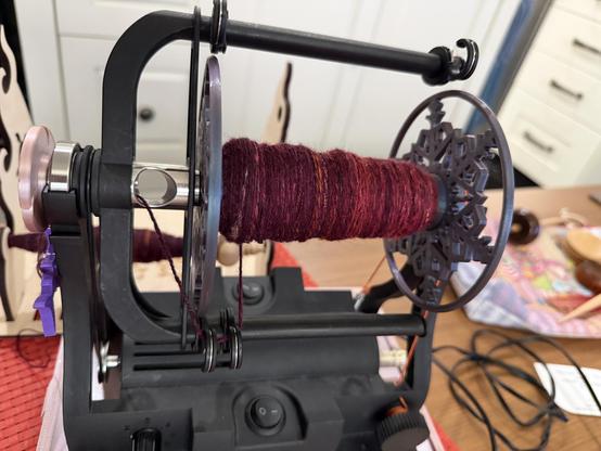Bobbin with the singles from first 2 of 3 spindles chain plied light red on right, darker red on left. On an EEW 6.1 e spinner.