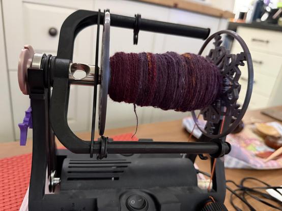 Bobbin with the singles from all 3 spindles chain plied shades of dark maroon and purple with hints of orange . On an EEW 6.1 e spinner.