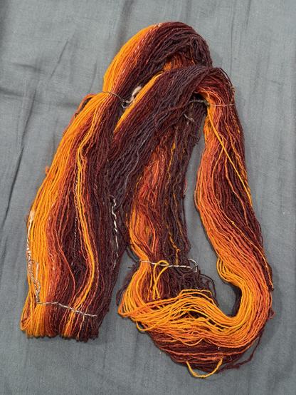 A skein of yarn - yellow orange though dark maroon / purple. Yarn is looped and tied and laying on a blue grey background