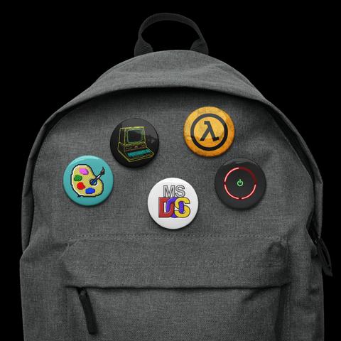 Promotional pic of a backpack with a set of five circular buttons:
A vectorized rendition of the MS Paintbrush icon; line art of the Commodore PET computer; the MS-DOS logo on white; A black Lambda sign on a grungy orange background; and the XBOX 360's "ring of death"