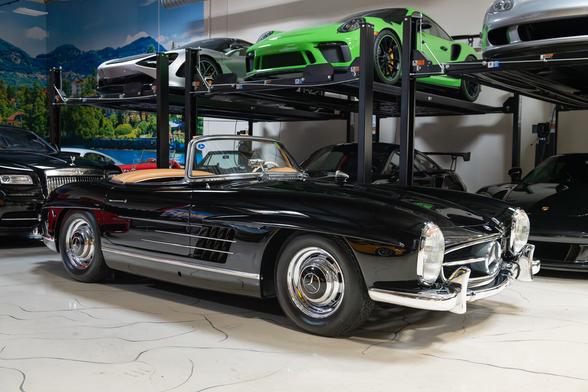 A black vintage convertible sits in front of a set of car lifts with various exotic cars on it.