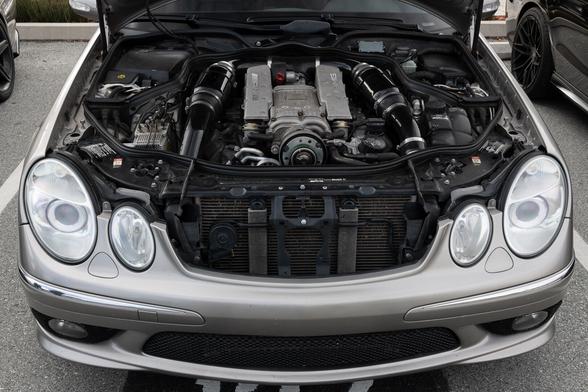 A silver car with oval headlights, its hood open, revealing a supercharged engine with custom intakes.