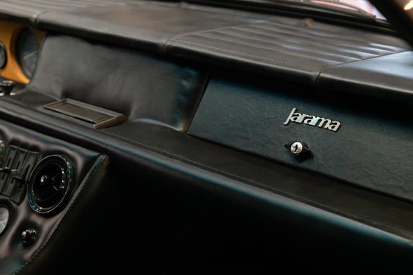 Black leather-clad dashboard. The logo “Jarama” appears in silver above the glove box opener.