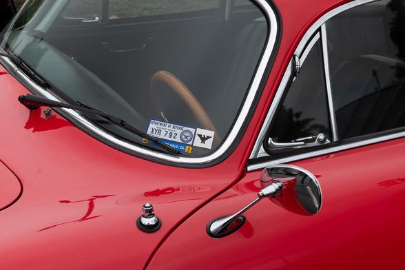 A-pillar detail of a red classic coupe. A Department of Defense parking sticker is on its windshield.