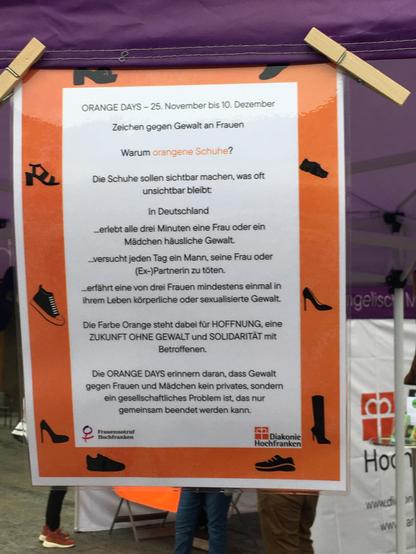 Ein kleines Plakat erklärt, was die orangen Schuhe ausdrücken sollen. Siehe tröt-Text