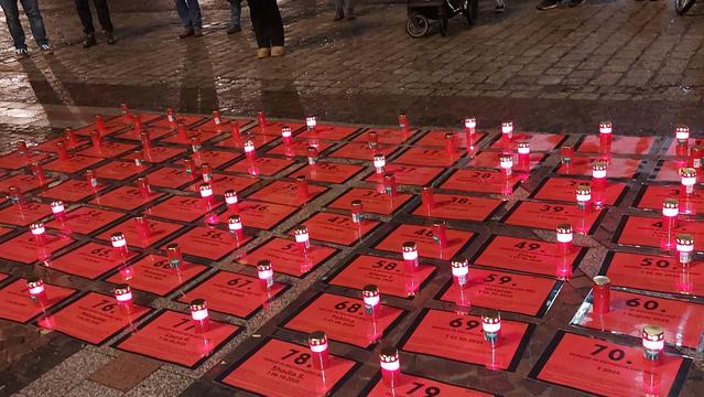 Rote Gedenktafeln mit Grabkerzen auf dem Boden.Wir gedenken 88 Frauen,die Opfer von Femiziden wurden.