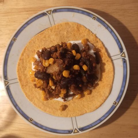 Ein Teller mit einer kleinen Tortilla. Drauf Tsatsiki und Veggie-Hack mit Bohnen, Mais, Chili und Zwiebeln