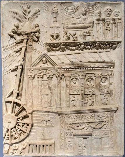 Description from the Musei Vaticani: The “relief shows a funerary monument in the form of a small temple: at the top the funeral bier can be seen; on the left appears what seems to be a machine used in its building, a sort of crane which is powered by a large wheel worked by slaves.“