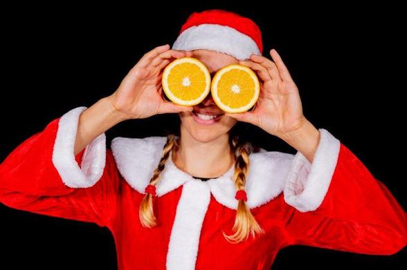 Eine Frau in Weihnachtskostüm hält sich zwei Orangenhälften vor die Augen und lächelt in die Kamera. © Physik im Advent
