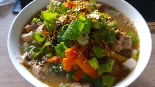 A white noodle bowl filled with ramen soup, lots of veggies, roast pork and some prawns. Delicious.