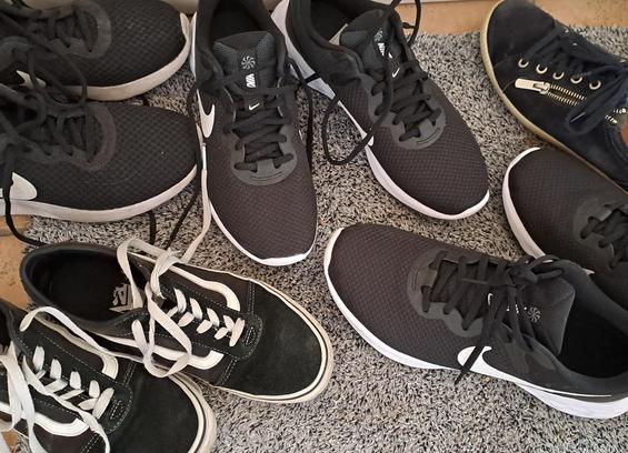Auf einer Fußmatte stehen paarweise, aber etwas durcheinander, acht schwarze Sportschuhe mit weißen Absetzungen. Ein einzelner dunkelblauer Schuh hat sich noch dazugesellt...