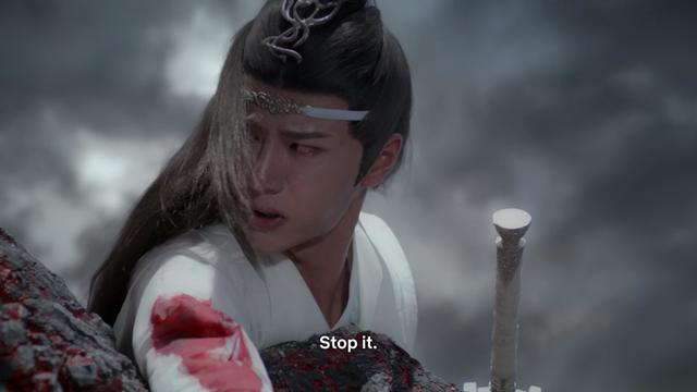 Lan Wangji lies on the ground at the edge of a cliff, his right arm extending out of frame down the cliffside. An injury to his upper arm has bled through his sleeve and down the arm. Wangji's head is turned to his right, face strained as he grits out to an offscreen Jiang Cheng:

Stop it.