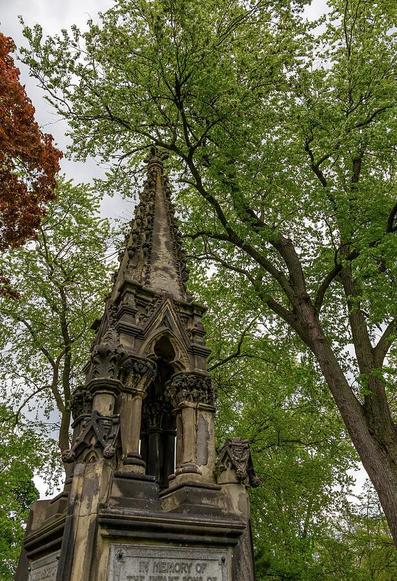 An ornate tombstone at the historic Toronto Necropolis, showcasing intricate Gothic design amidst autumn foliage.