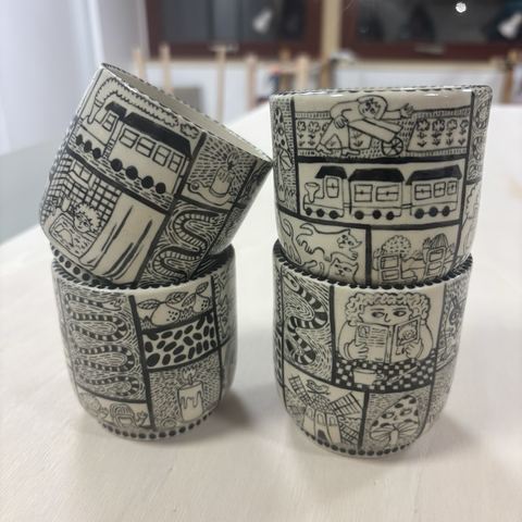 Photo de quatre petites tasses sans anses décorées de dessins en noir et blanc dans des petites cases représentants différentes scènettes, personnages et objets.
