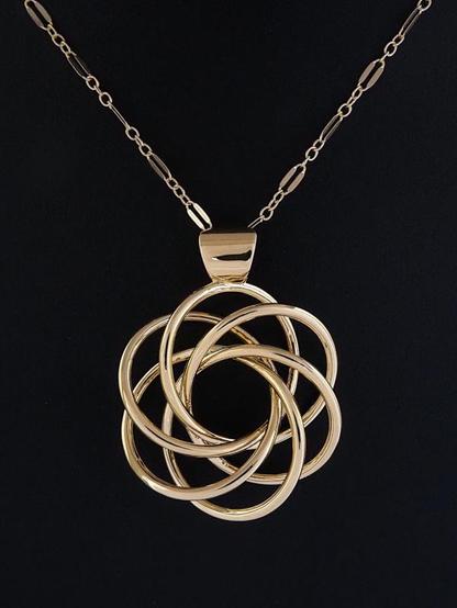 Photograph of Harmonia, a shiny 1-3/8 in (35mm) gold-plated brass pendant in the looping shape of a stylized flower with six petals. The piece has a shiny inverted trapezoidal bail fitted with a gold long-and-short loop chain and sits on a black background.