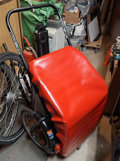 Die rote Lkw-Plane mit dem gespannten Gummiband ist über die Wanne eines Donkey-Einkaufsanhänger gespannt. Der Anhänger steht in einem engen Kellerraum