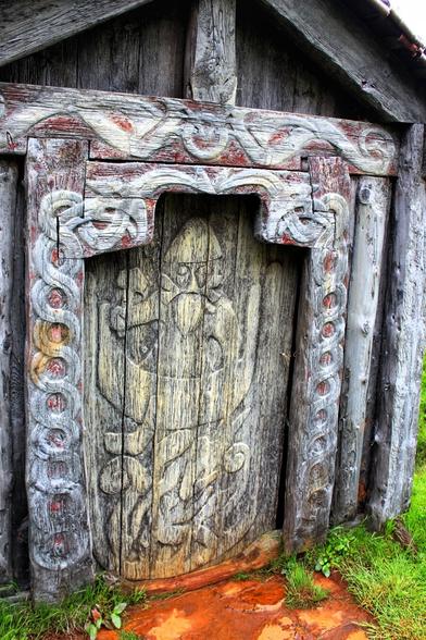 A wooden door. Artistic carvings are on the door and the frame. Looking very cliché viking.