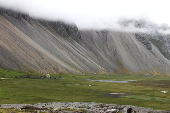 Even further away. The village lies in green on the foot of the mountain. The mountain dwarfs the village.