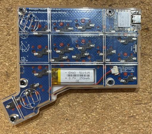 Underside of the left hand’s half of the ‘Forager Acid’ split keyboard, with a transparent bottom case letting you see the blue PCB, LiPo battery (bottom middle), hot swap switch sockets, and Seeed Xiao controller (top right).