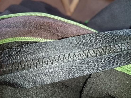 A new black zipper with big plastic teeth is on top of a black jacket with an old green zipper with small teeth.