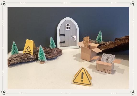 Foto einer grauen Wichteltür. Daneben Baumrinde, kleine Umzugskartons, Tannenbäume und Baustellenschilder.