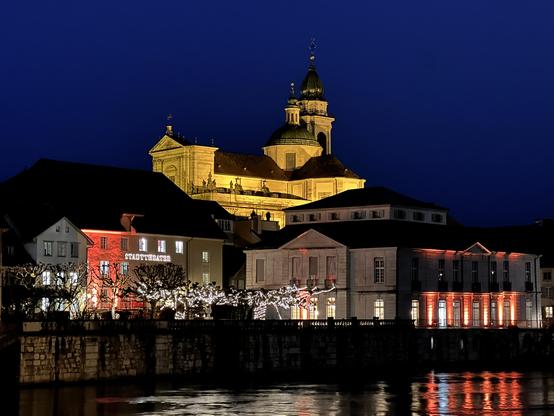 St-Ursen-Kathedrale in Solothurn in der Nacht mit der schön beleuchteten Häuser-Front an der Aare.