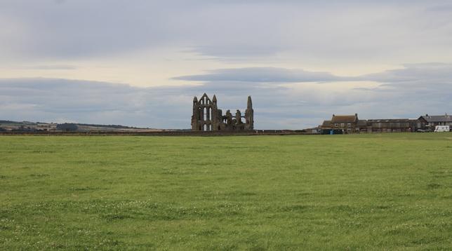 Une grande étendue d’herbe et les ruines d’une abbaye qui se détachent sur le ciel gris.