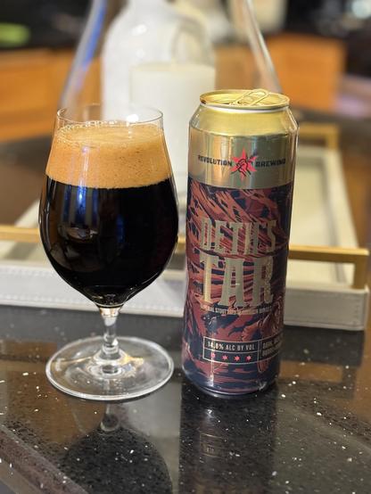 A tall snifter glass full of dark beer is next to an equally tall pint-and-then-some can. The can has a gold top and rippled dark brown lower section. A line of four red stars marks the bottom.
