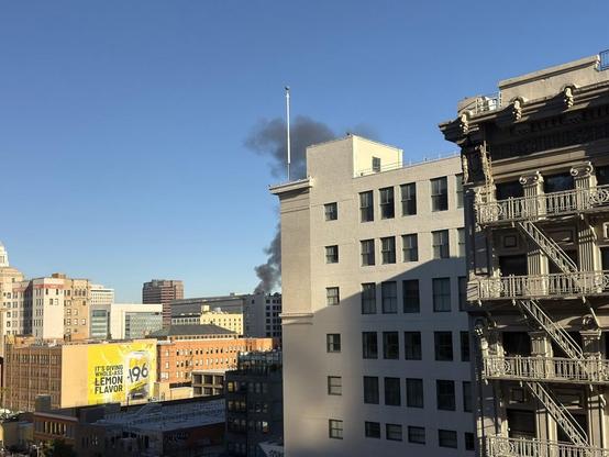 A plume of dark smoke rising up from behind buildings in downtown Los Angeles.
