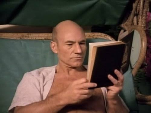 Picard reading a book in a lounge chair wearing a swimsuit