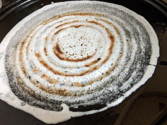 Dosa getting cooked with the batter crisp and browned where thin as it was spread on the griddle