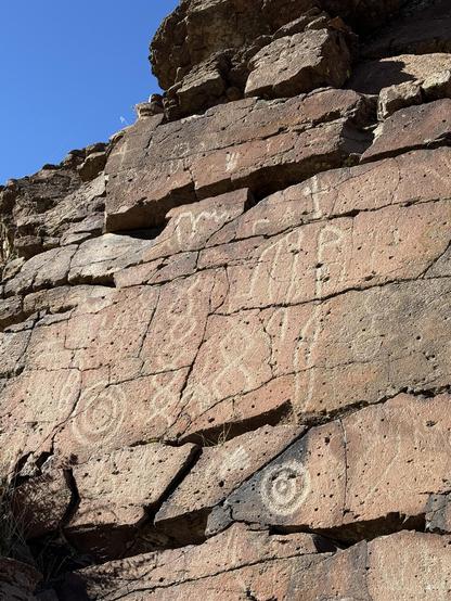 Very clear petroglyphs on a reddish sandstone walls. Blue sky above.