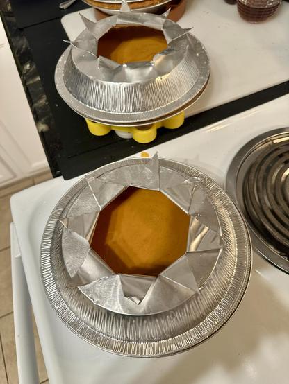 A few pumpkin pies in the foil pans, ready to load into the oven. The foil pans upside down on top of each pie are slit into a 8 sided star shape so I could bend back the star points to expose the center of each pie to heat better without burning the crust on the edge of each pan.