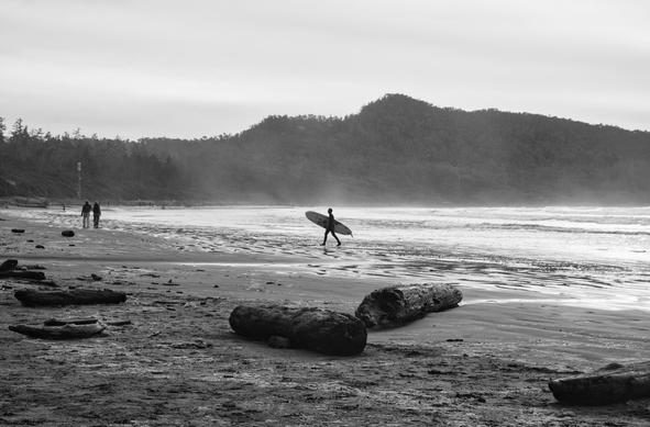 Black and white of beach with surfer walking out of the water with their board.